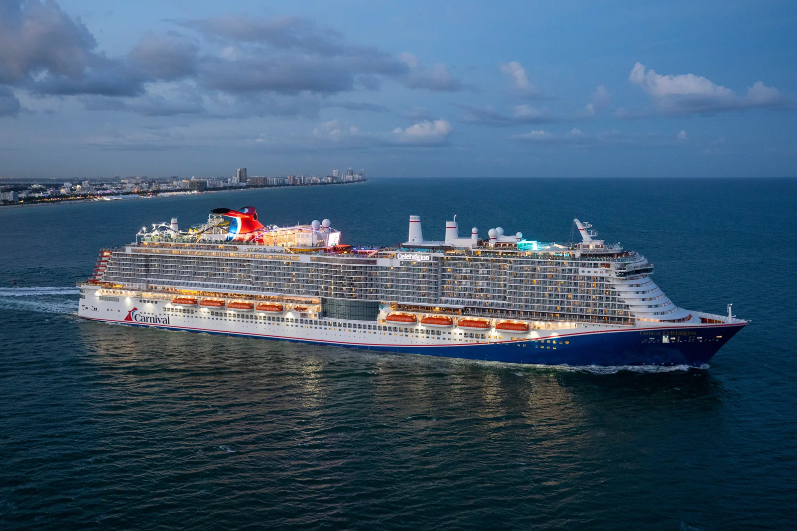 Carnival Celebration departing Miami at golden hour with the city skyline visible behind the ship